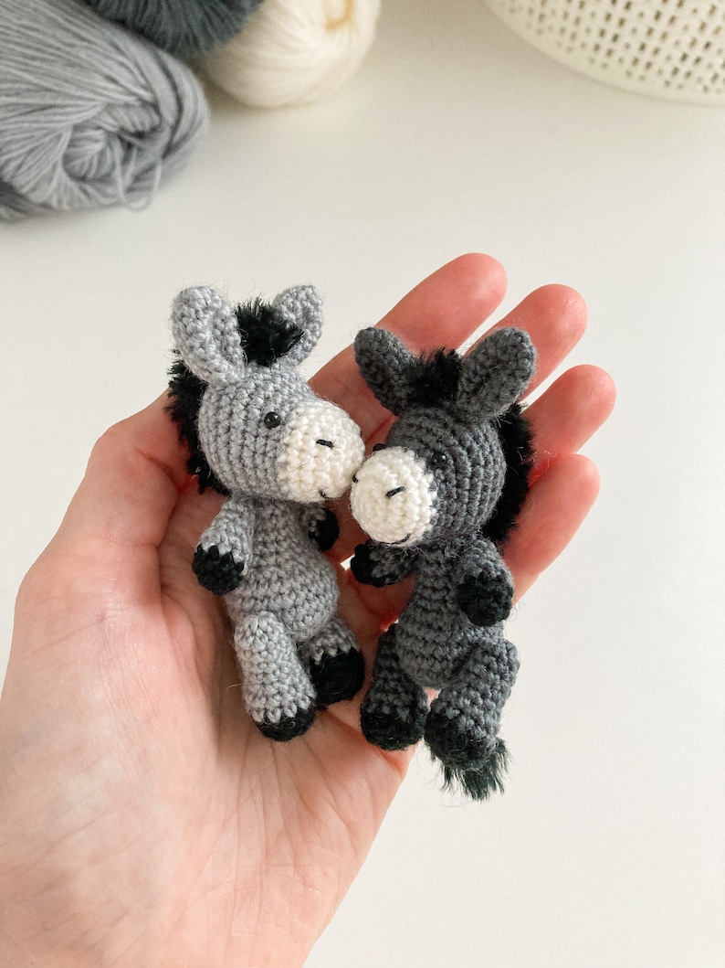 May include: Two gray crocheted donkey figurines with black manes and tails. The donkeys are facing each other and have white faces.