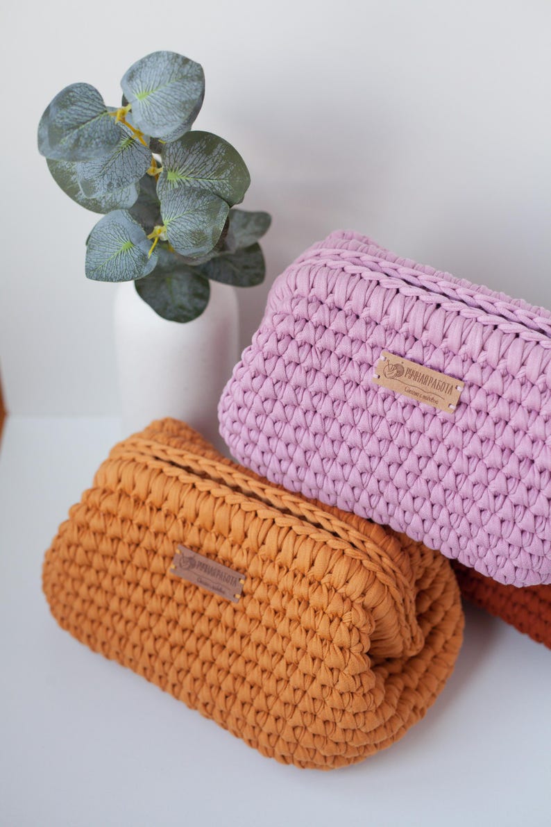 May include: Two crocheted pouches in orange and pink with a brown leather tag that says "PRIMAVERA" on them. The pouches are stacked on top of each other.