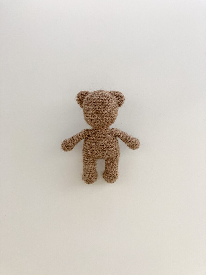 K&ouml;nnte beinhalten: Ein brauner H&auml;kelteddyb&auml;r mit schlichtem Design. Der B&auml;r steht auf einem wei&szlig;en Hintergrund.