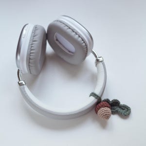 May include: White headphones with a gray headband and a crocheted acorn charm attached to the headband.