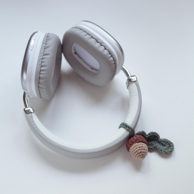 May include: White headphones with a gray headband and a crocheted acorn charm attached to the headband.