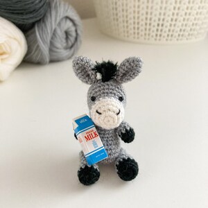 May include: A gray crocheted donkey holding a miniature carton of milk that says "Fresh Milk".
