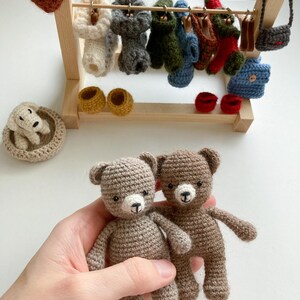 May include: Two brown crocheted teddy bears with white faces and black eyes. The bears are being held in a hand.
