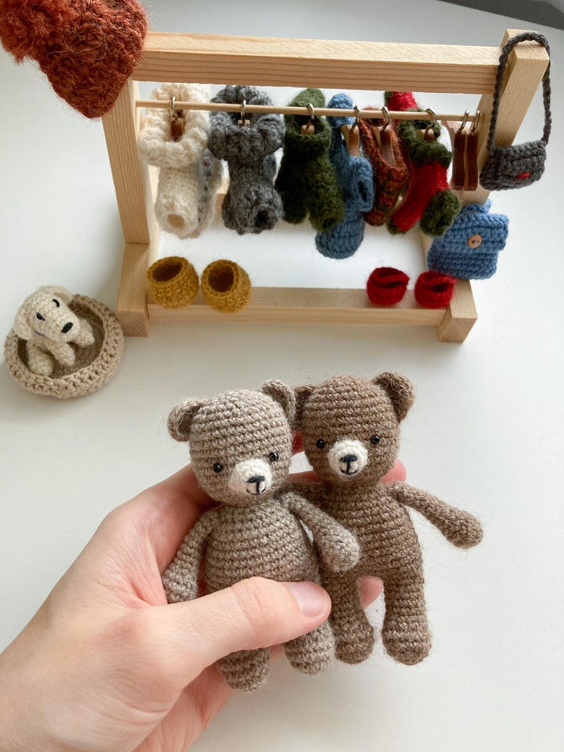 May include: Two brown crocheted teddy bears with white faces and black eyes. The bears are being held in a hand.