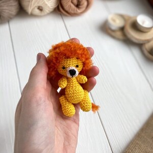 K&ouml;nnte beinhalten: Ein kleines geh&auml;keltes L&ouml;wenspielzeug mit gelbem K&ouml;rper, orangefarbener M&auml;hne und schwarzen Augen. Der L&ouml;we wird in der Hand einer Person gehalten.