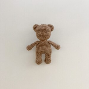 May include: A brown crocheted teddy bear toy with a simple design. The bear is standing on a white background.