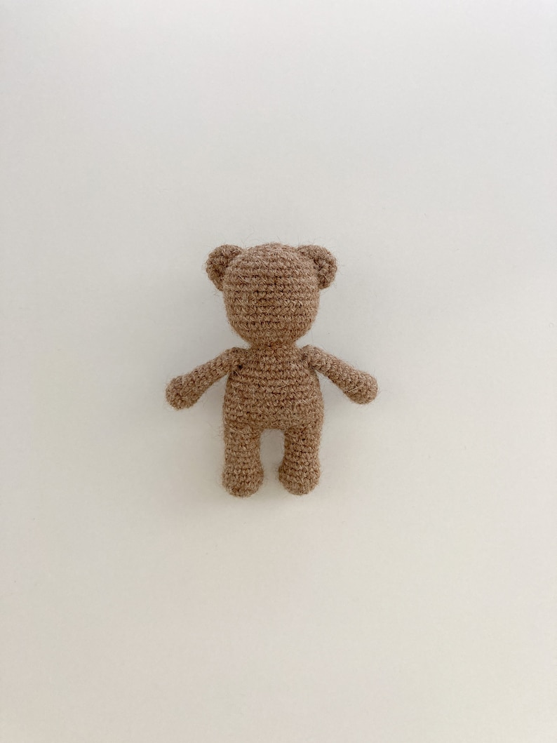May include: A brown crocheted teddy bear toy with a simple design. The bear is standing on a white background.