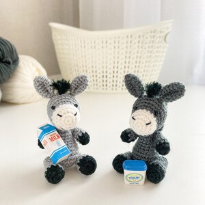 May include: Two gray crocheted donkey figurines, one holding a miniature carton of milk labeled "Fresh Milk", the other holding a miniature container of yogurt labeled "Natural Yogurt Plus".