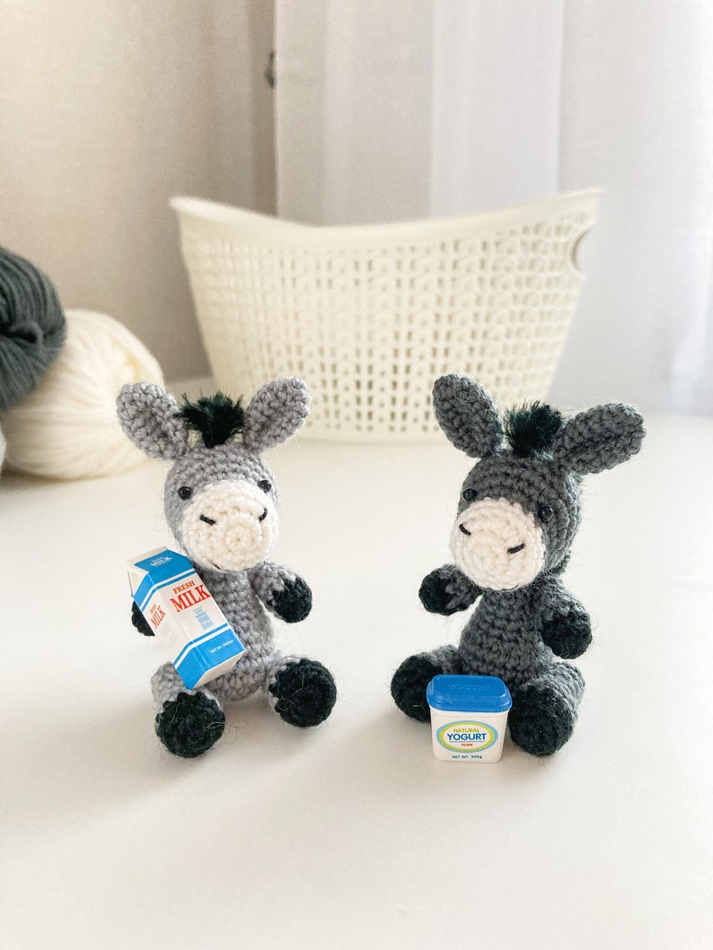 May include: Two gray crocheted donkey figurines, one holding a miniature carton of milk labeled "Fresh Milk", the other holding a miniature container of yogurt labeled "Natural Yogurt Plus".