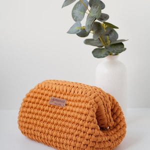 May include: A crocheted mustard yellow pouch with a brown leather tag that says "OPRAHMAGLIA".