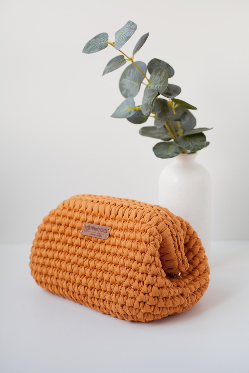 May include: A crocheted mustard yellow pouch with a brown leather tag that says "OPRAHMAGLIA".