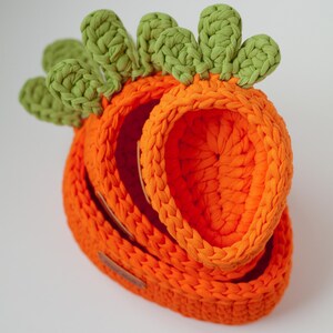 May include: A set of three orange crocheted baskets shaped like carrots with green crocheted tops.