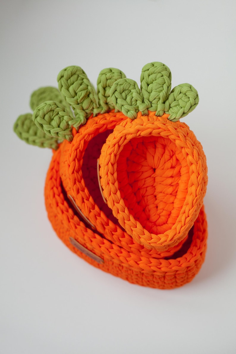 May include: A set of three orange crocheted baskets shaped like carrots with green crocheted tops.