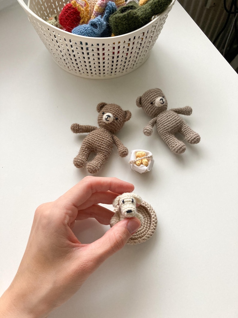 May include: Two brown crocheted teddy bears, a white crocheted dog in a brown crocheted bed, and a small white box with gold accents.