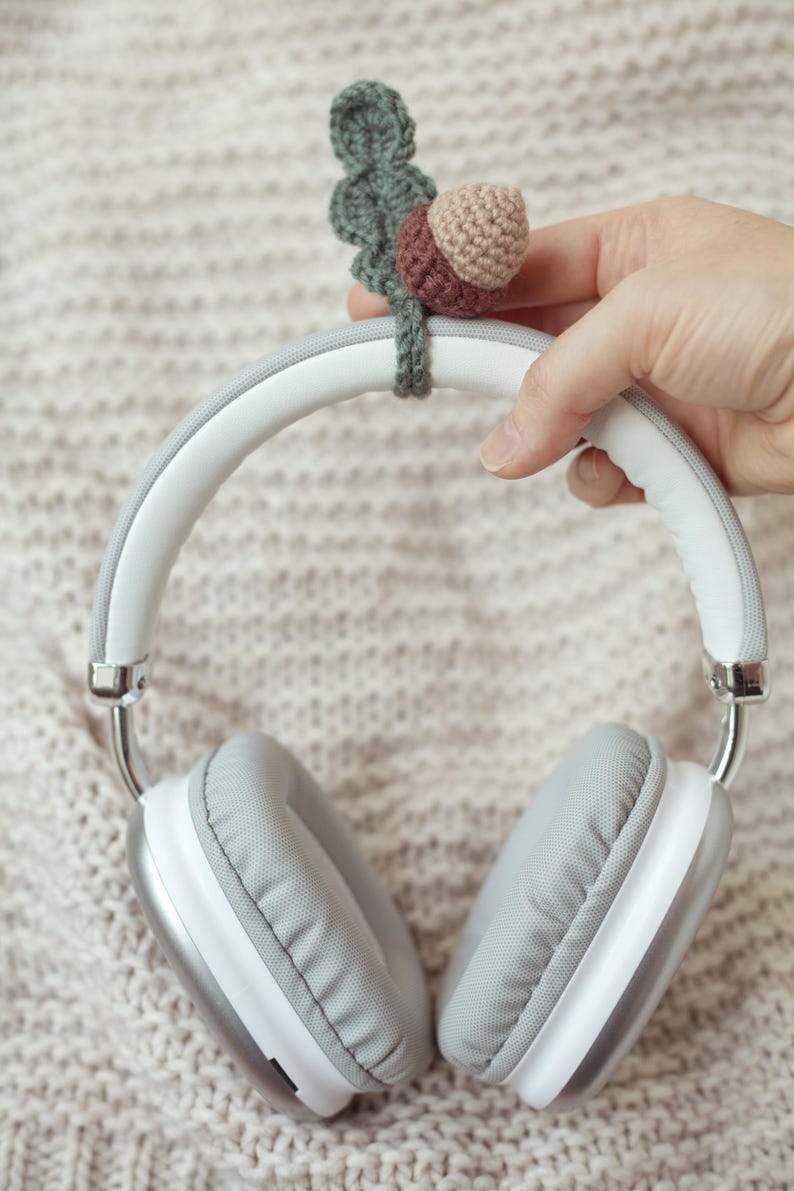 May include: White headphones with gray earcups and a crocheted acorn charm attached to the headband.