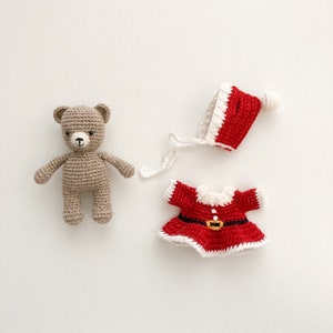 K&ouml;nnte beinhalten: Ein geh&auml;kelter Teddyb&auml;r, der eine rot-wei&szlig;e geh&auml;kelte Weihnachtsm&uuml;tze und ein rotes geh&auml;keltes Kleid mit einem schwarzen G&uuml;rtel tr&auml;gt.
