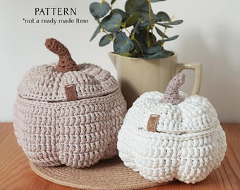 May include: Two crocheted pumpkin-shaped baskets with lids. The larger basket is beige and the smaller basket is white. Both baskets have a brown leather tag with the word "love" on them.
