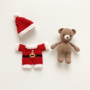 K&ouml;nnte beinhalten: Ein brauner geh&auml;kelter Teddyb&auml;r, der einen roten geh&auml;kelten Weihnachtsmann-Anzug mit wei&szlig;em Besatz und einem schwarzen G&uuml;rtel tr&auml;gt. Der Teddyb&auml;r tr&auml;gt eine rote geh&auml;kelte Weihnachtsmannm&uuml;tze mit einem wei&szlig;en Bommel.