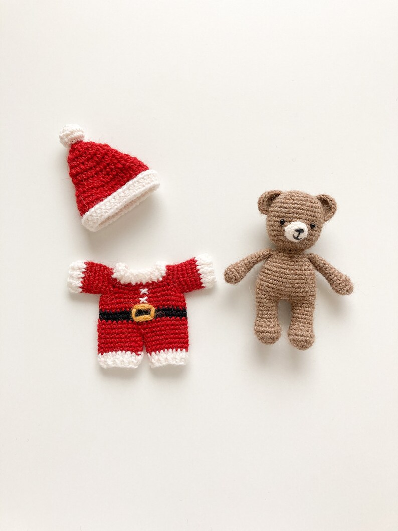 K&ouml;nnte beinhalten: Ein brauner geh&auml;kelter Teddyb&auml;r, der einen roten geh&auml;kelten Weihnachtsmann-Anzug mit wei&szlig;em Besatz und einem schwarzen G&uuml;rtel tr&auml;gt. Der Teddyb&auml;r tr&auml;gt eine rote geh&auml;kelte Weihnachtsmannm&uuml;tze mit einem wei&szlig;en Bommel.