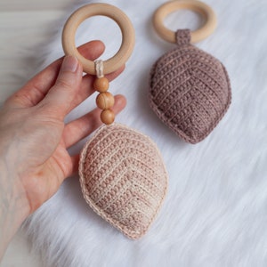 May include: Two crocheted leaf-shaped teethers with wooden rings and beads. The teethers are in shades of pink and brown.