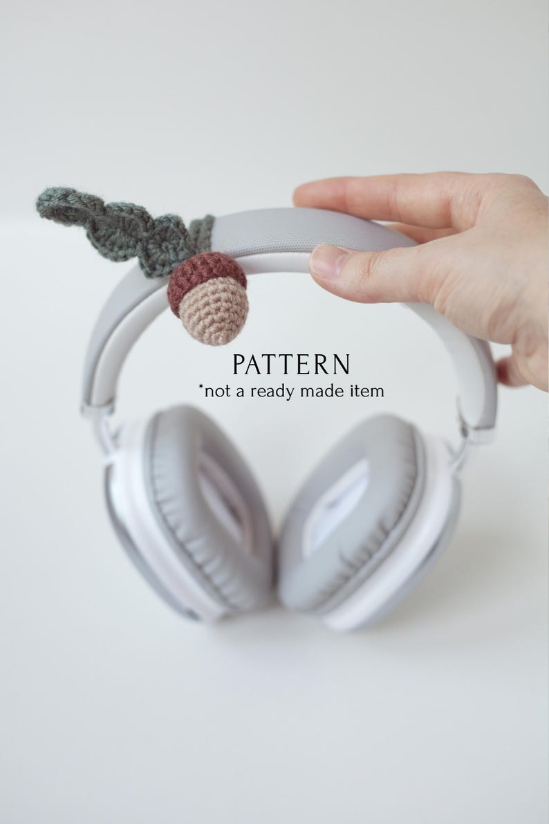 May include: A crocheted acorn charm with green leaves attached to a pair of gray headphones. The text "PATTERN *not a ready made item" is visible below the headphones.