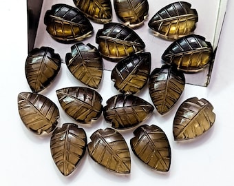 May include: A collection of 18 smoky quartz leaf-shaped cabochons. The cabochons are carved with a detailed leaf pattern and have a translucent, smoky brown color.
