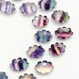 May include: A collection of 12 iridescent, faceted, oval-shaped fluorite gemstones. The fluorite is a mix of purple, green, and white.