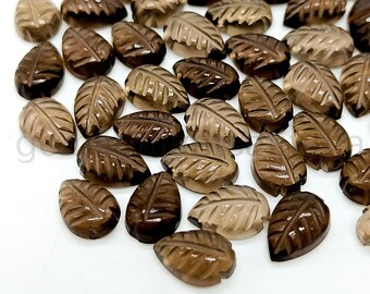May include: A collection of smoky quartz leaf-shaped cabochons. The stones are a translucent brown color and have a carved leaf design.