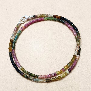 May include: A multi-colored gemstone necklace with a silver clasp. The necklace is made of small, round beads in shades of pink, green, black, and brown.
