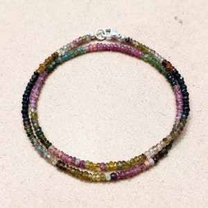 May include: A multi-colored gemstone necklace with a silver clasp. The necklace is made of small, round beads in shades of pink, green, blue, and black.