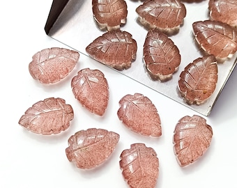 May include: A collection of pink and clear leaf-shaped gemstone cabochons. The cabochons are arranged on a silver tray and a white surface.