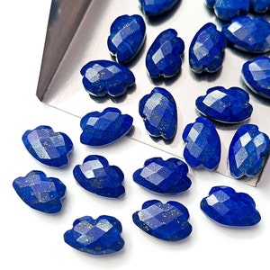 Pode incluir: Uma coleção de pedras preciosas de lápis-lazúli azul profundo facetadas. As pedras preciosas têm várias formas, incluindo desenhos em forma de nuvem e lágrima. As pedras têm uma superfície polida e refletora com manchas douradas. Estão dispostas numa bandeja prateada.