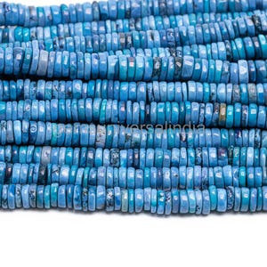 Op de afbeelding: Close-up van strengen blauwe edelsteen kralen. De kralen zijn plat, schijfvormig en variëren in blauwtinten, van licht tot diep turkoois. De kralen zijn aan elkaar geregen, waardoor een textuur ontstaat.