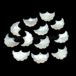 May include: A collection of 12 white moonstone cabochons, each shaped like a crescent moon. The stones are faceted and have a pearly sheen.