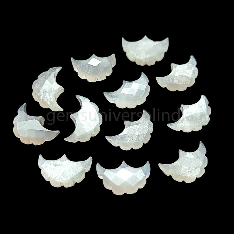May include: A collection of 12 white moonstone cabochons, each shaped like a crescent moon. The stones are faceted and have a pearly sheen.