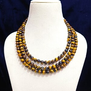 May include: A triple strand necklace made of tiger's eye beads. The beads are a mix of golden brown and black.