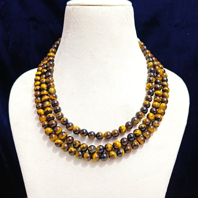 May include: A triple strand necklace made of tiger's eye beads. The beads are a mix of golden brown and black.