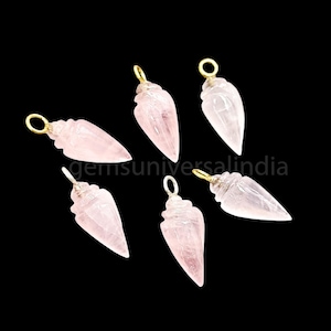 May include: Six rose quartz crystal pendants with gold-colored metal loops. Each pendant is a light pink color, with a pointed, teardrop shape. The pendants are displayed against a black background.