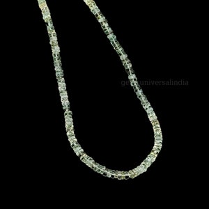 May include: A strand of light green gemstone beads, strung together to form a necklace. The beads are faceted and have a subtle shimmer.