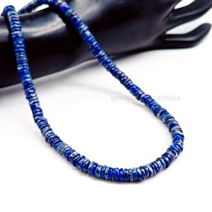 May include: A strand of deep blue lapis lazuli beads, each bead is a flat, round disc with a slightly irregular shape. The beads are strung on a clear thread and are arranged in a simple, elegant design.