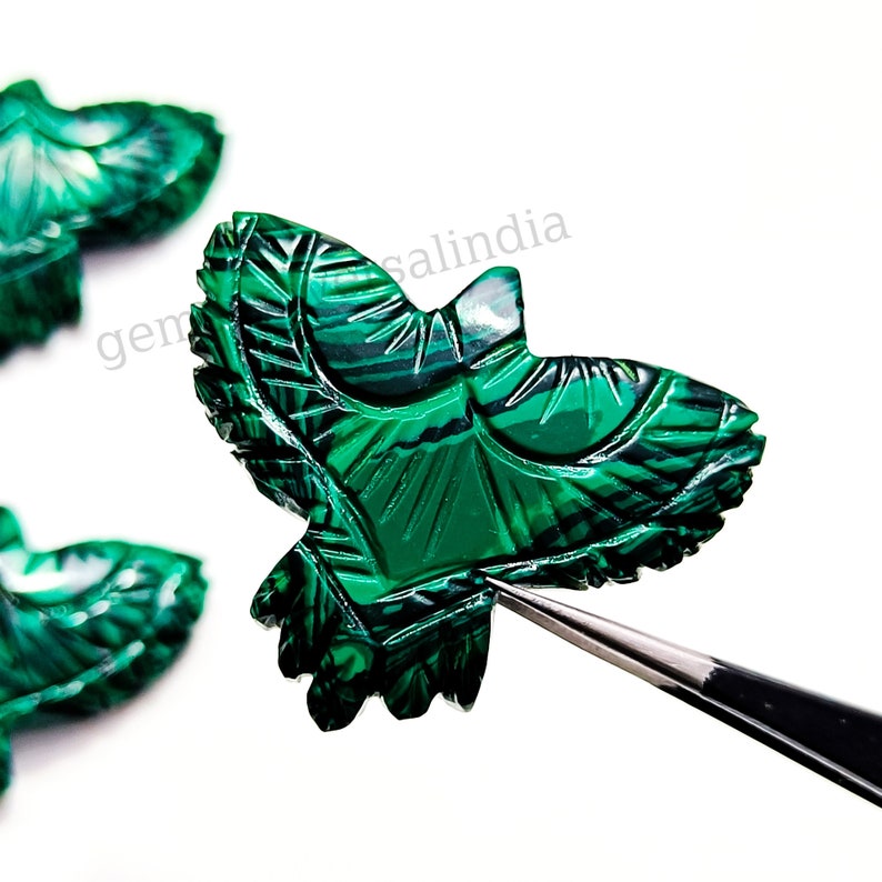 May include: Green malachite gemstone carved into the shape of a bird. The bird is detailed with intricate carvings and has a glossy finish.