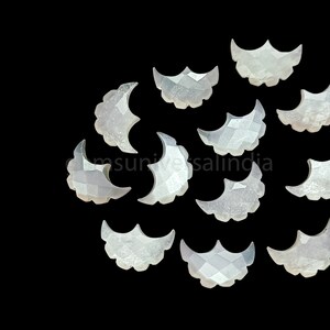 May include: A collection of 12 white, crescent moon shaped, mother of pearl gemstone cabochons. The cabochons are faceted and have a slightly iridescent sheen.