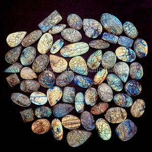 May include: A collection of carved labradorite gemstones in various shapes and sizes. The stones are iridescent with shades of blue, green, and gold. The carvings feature intricate floral designs.
