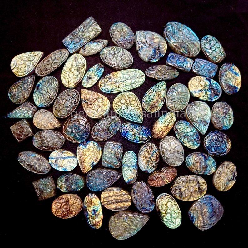 May include: A collection of carved labradorite gemstones in various shapes and sizes. The stones are iridescent with shades of blue, green, and gold. The carvings feature intricate floral designs.