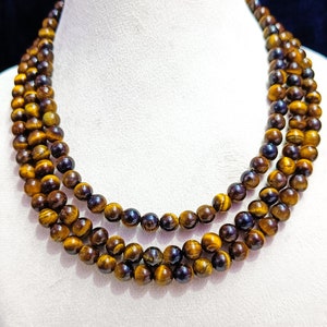 May include: A triple strand necklace made of tiger's eye beads. The beads are a mix of golden brown and black.