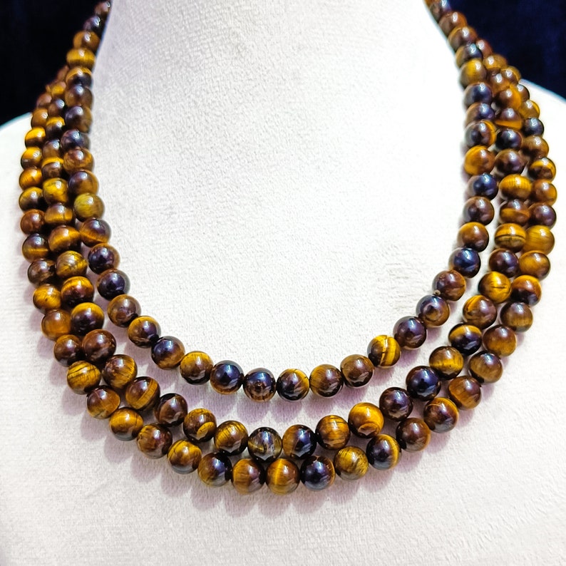 May include: A triple strand necklace made of tiger's eye beads. The beads are a mix of golden brown and black.