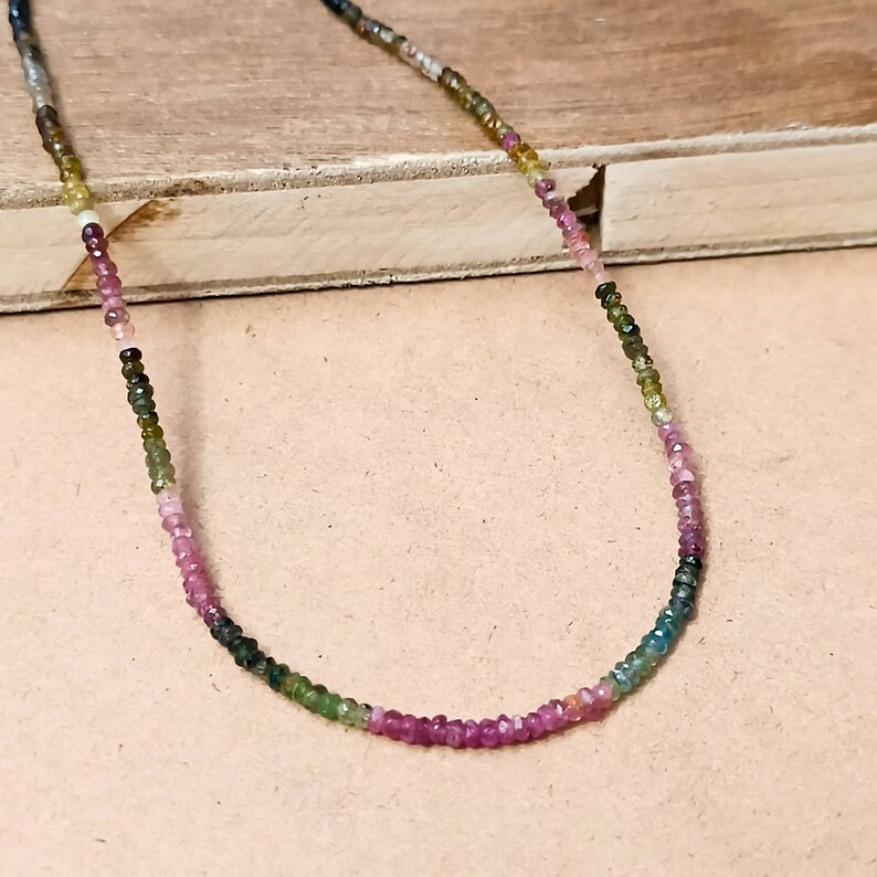 May include: A multi-colored gemstone necklace with small, round beads in shades of pink, green, and blue.