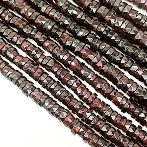 May include: A strand of dark red faceted gemstone beads. The beads are cylindrical and have a faceted, almost starburst-like, design. The beads are strung on a clear thread.