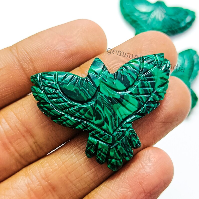 May include: Green malachite stone carved into the shape of a bird. The bird has detailed wings and a long tail. The stone has a natural marbled pattern.