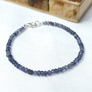 May include: A delicate bracelet made with small, faceted, dark blue gemstones. The bracelet has a silver clasp.